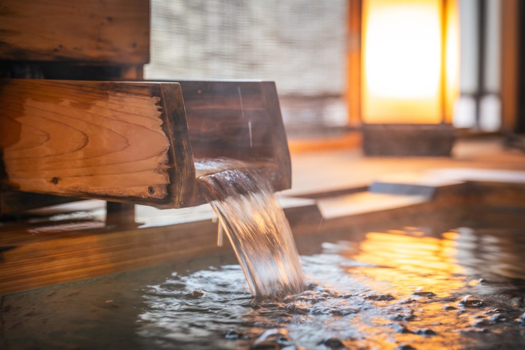 Traditional Japanese hot spring bath with wooden water spout and warm ambient lighting