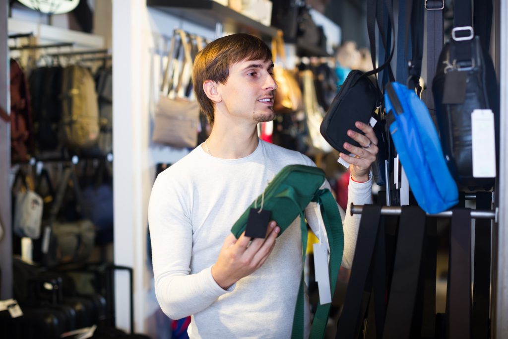 Ordinary young man buying textile purse in haberdashery shop