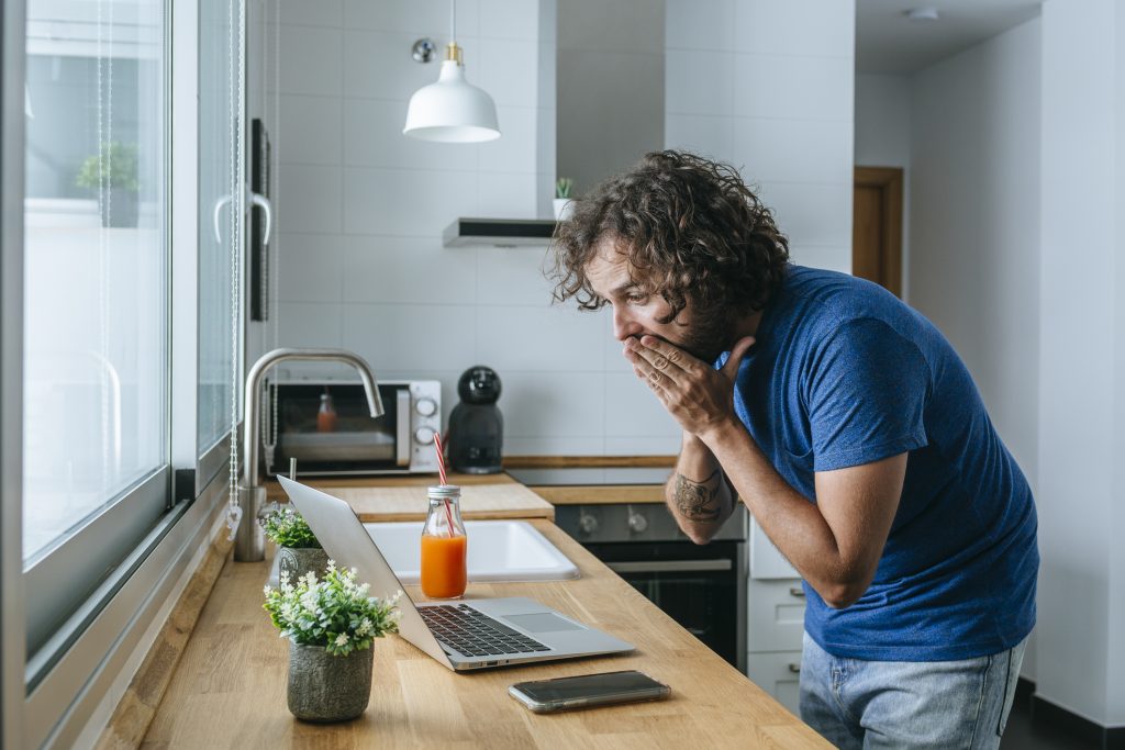 Man looking at laptop surprised at home