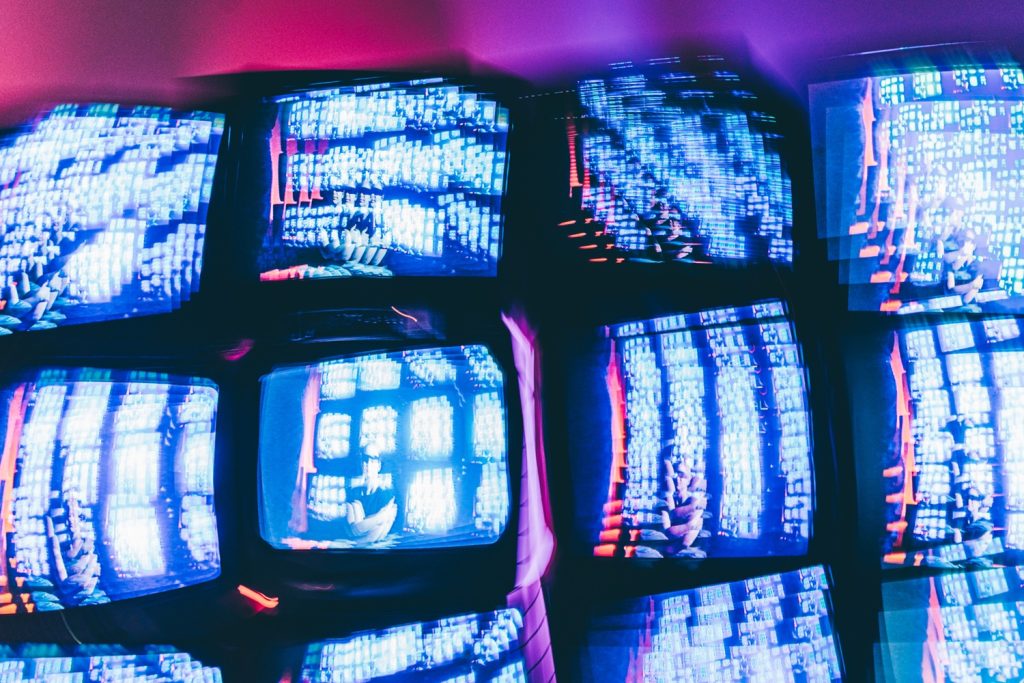 Online privacy violations. Big brother is behind you. Several TVs against a neon wall.